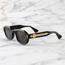 An image of the Palace Cutler and Gross Victory Round Sunglasses in Black frame side view with arms open marble background