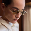 Female model wears Cutler and Gross titanium oval sunglasses in gold