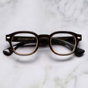 An image of the Cutler and Gross 9290 Round Horn Optical in Smoke Brown/Cream Buffalo Horn frame frontal view with arms closed marble background