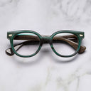 An image of the Cutler and Gross 9298 Round Horn Optical in Moss Green/Brown Buffalo Horn frame frontal view with arms closed marble background