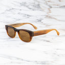 An image of the Cutler and Gross 0425 Rectangular Horn Sunglass in Toasted Brown Buffalo Horn frame side view with arms open marble background