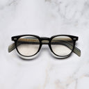 An image of the GR09 Round Optical Glasses in Black on Horn frame frontal view with arms closed marble background