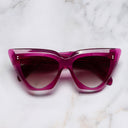 An image of the 1407 Cat Eye Sunglasses in Fuchsia frame frontal view with arms closed marble background