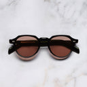An image of the GR06 Round Sunglasses in Black frame frontal view with arms closed marble background