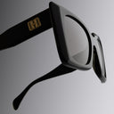 An image of the Cutler and Gross Akira 001 Cat Eye Sunglasses in Black frame with Black lenses detail close up of right lens and right temple with gold logo.