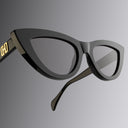 Black cat-eye sunglasses with gold accents on a gradient gray background