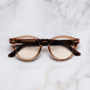 An image of the 1378 Blue Light Filter Optical Round Glasses (Small) in Crystal Peach on Striped Brown frame frontal view with arms closed marble background