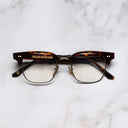 An image of the 0004 Kingsman Optical Round Glasses in Dark Turtle frame frontal view with arms closed marble background