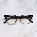 An image of the 0004 Kingsman Optical Round Glasses in Classic Navy Blue frame frontal view with arms closed marble background