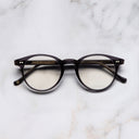 An image of the 0710 Kingsman Optical Round Glasses in Dark Grey frame frontal view with arms closed marble background