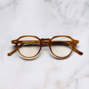 An image of the 1313 Kingsman Optical Round Glasses in Striped Mustard Havana frame frontal view with arms closed marble background