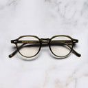 An image of the 1313 Kingsman Optical Round Glasses in Olive frame frontal view with arms closed marble background