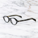 An image of the GR13 Oval Opticals in Black Horn frame side view with arms open marble background