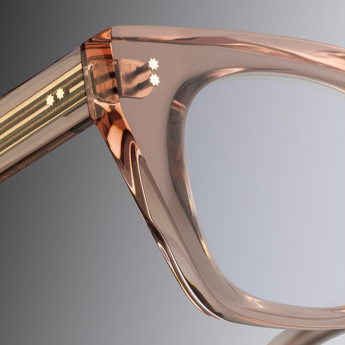 Close-up of a transparent  optical frame in blush colour on a gray background, Cutler and Gross, featuring specific to cutler and gross campus pins