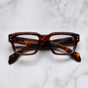 An image of the 1432 Square Optical in Dark Turtle frame frontal view with arms closed marble background