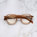 An image of the GR06 Round Optical Glasses in Crystal Peach frame frontal view with arms closed marble background 