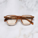 An image of the GR07 Square Optical Glasses in Crystal Peach frame frontal view with arms closed marble background