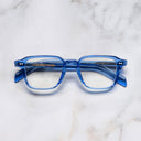 An image of the GR07 Square Optical Glasses in Blue Crystal frame frontal view with arms closed marble background 