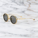 An image of the Cutler and Gross 1438 in Black/Gold frame side view with arms open in marble background.