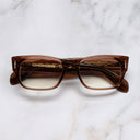 An image of the The Great Frog Dagger Square Optical Glasses in Cola Crystal frame frontal view with arms closed marble background 