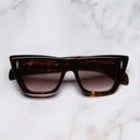 An image of the The Great Frog Love And Death Cat Eye Sunglasses in Black Turtle frame frontal view with arms closed marble background 