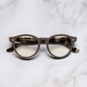 An image of the 1378 Blue Light Filter Optical Round Glasses (Small) in Mud on Jet Engine Grey frame frontal view with arms closed marble background 