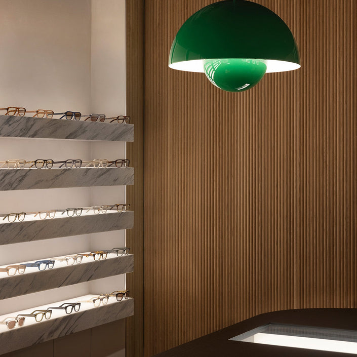 Green pendant light hanging in a room with shelves displaying eyeglasses.