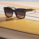 Image of the Breitling Marisol 0005 Square Sunglasses in Black on a yellow surfboard. 