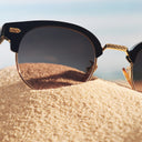 Close up image of Breitling Biarritz 0003 Round Sunglasses Limited Edition on the sand, with only the right lens showing.