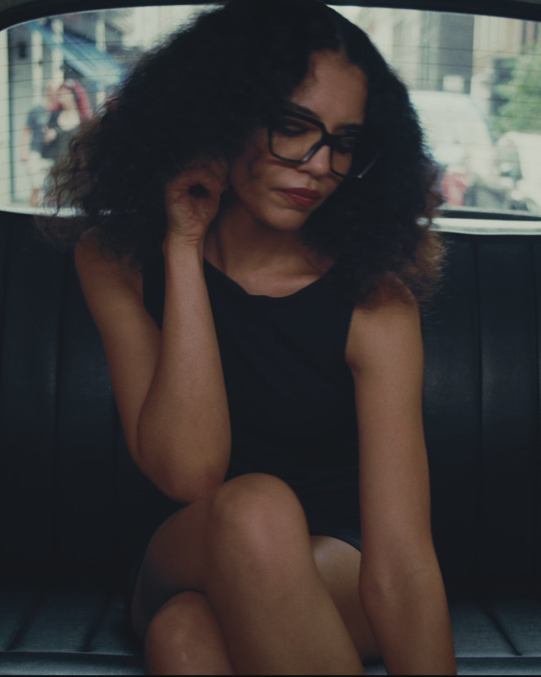 A video of a woman with curly hair wearing oversized Cutler and Gross optical frame in the back of a black cab in London.
