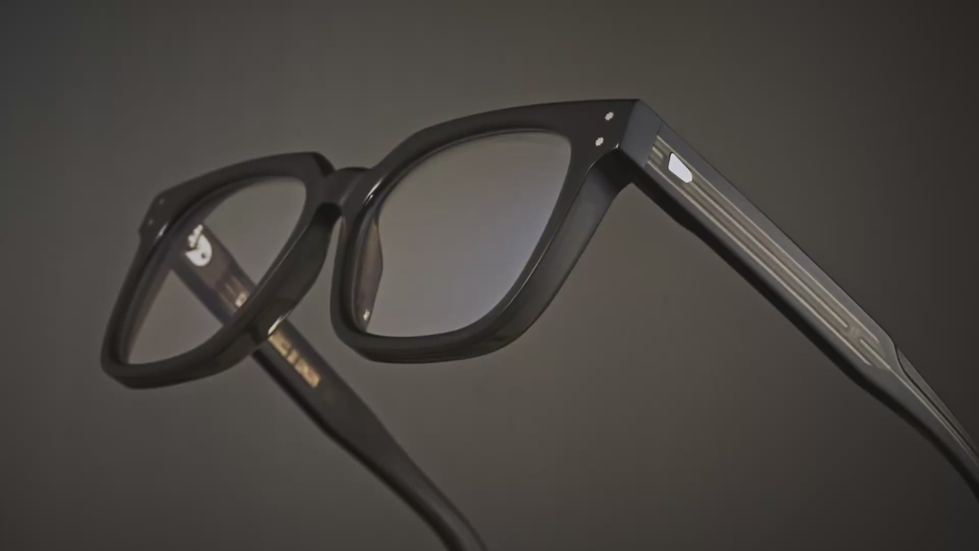 A 360 degree video of the Cutler and Gross 9387 Square Optical frame in Olive colourway with a close up view of details on temples and lenses in a olive and grey background.